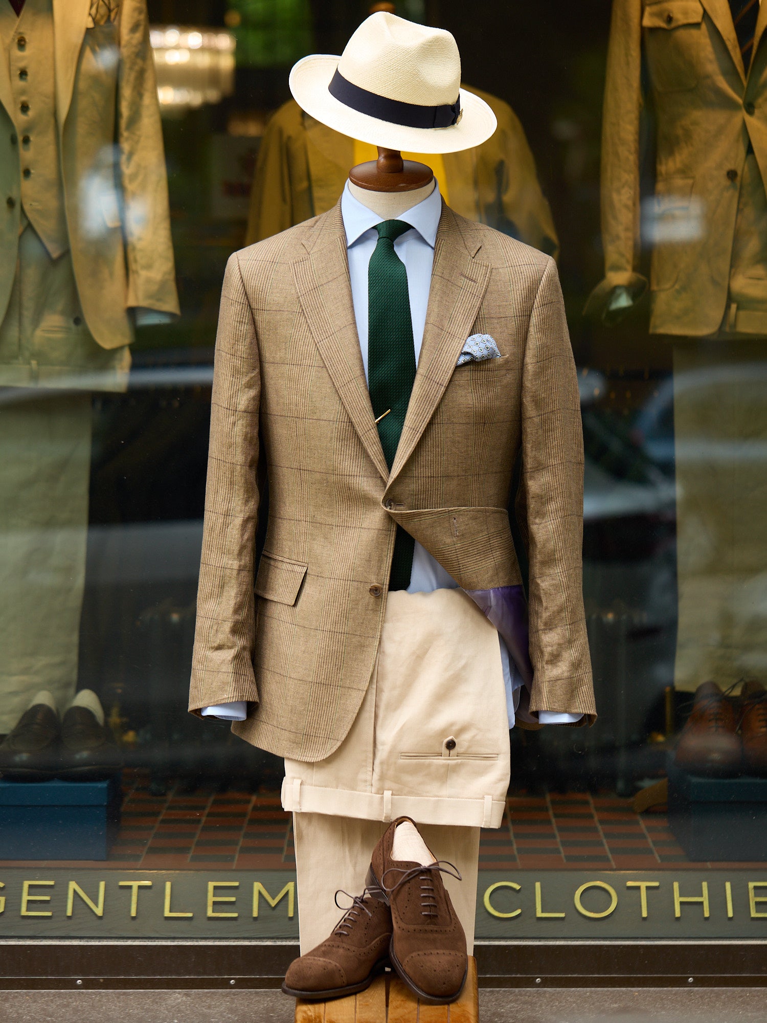 Mannequin wearing a stylish suit with a hat in front of a store window display.